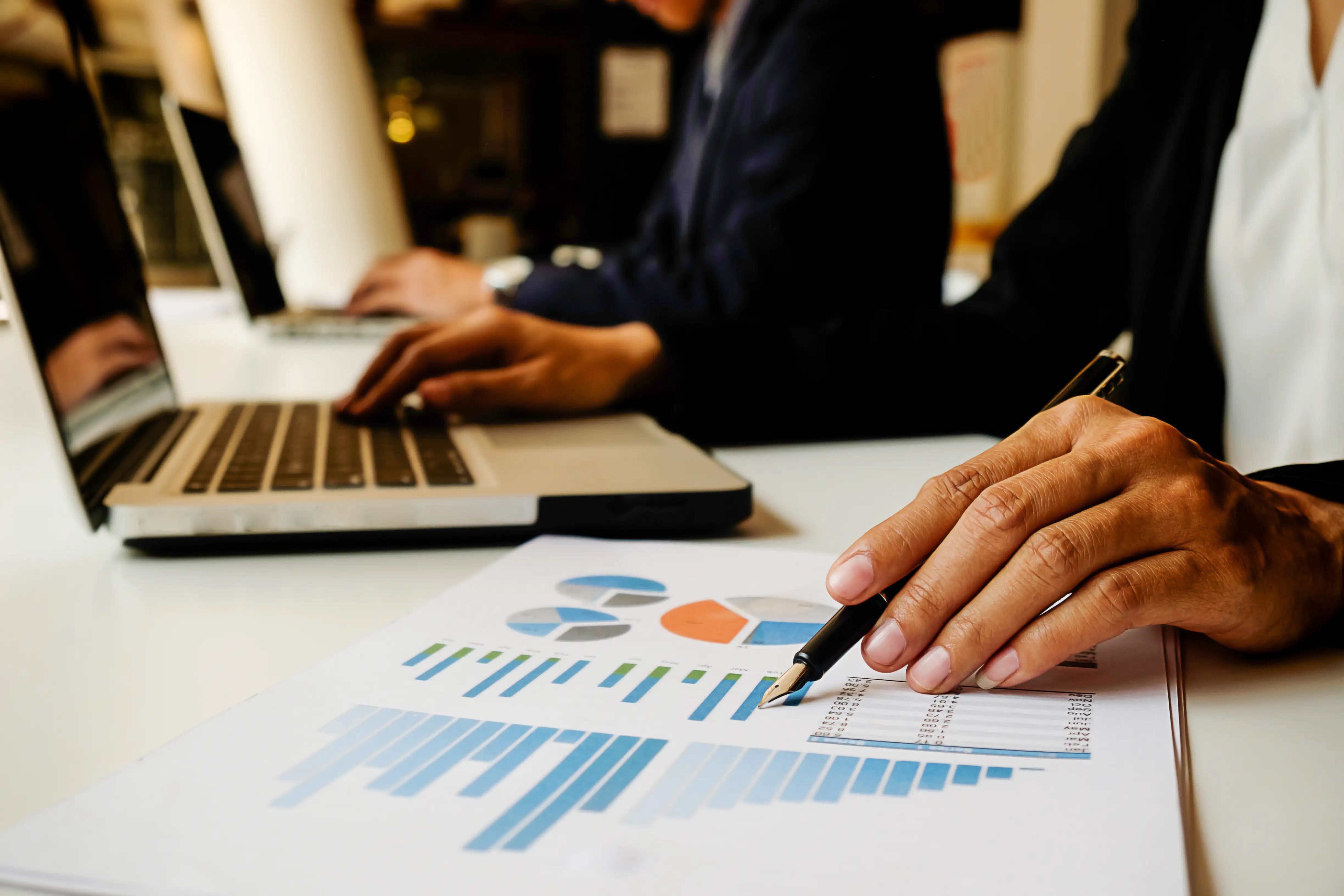 Analista apontando para gráficos de desempenho financeiro ao lado de um laptop