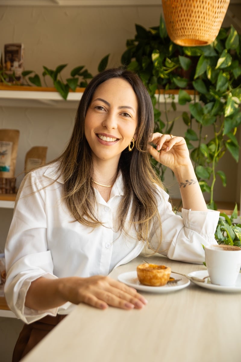 Thalia Cardoso de camisa branca, sorrindo em uma cafeteria.
