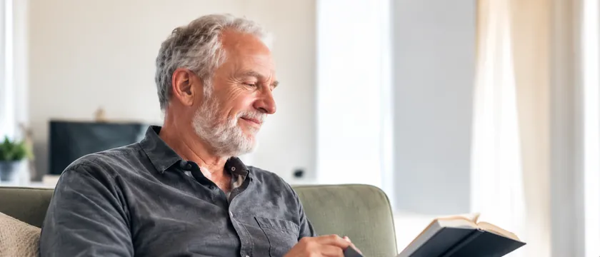Homem de cabelos grisalhos lendo um livro em casa