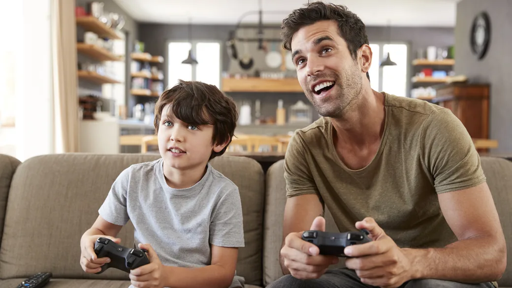 Pai e filho jogando videogame no sofá