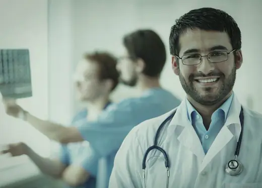 Médico sorrindo com colegas ao fundo, em foto com filtro esverdeado