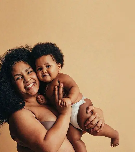 Mulher sorrindo com o bebê no colo, fundo em tom quente