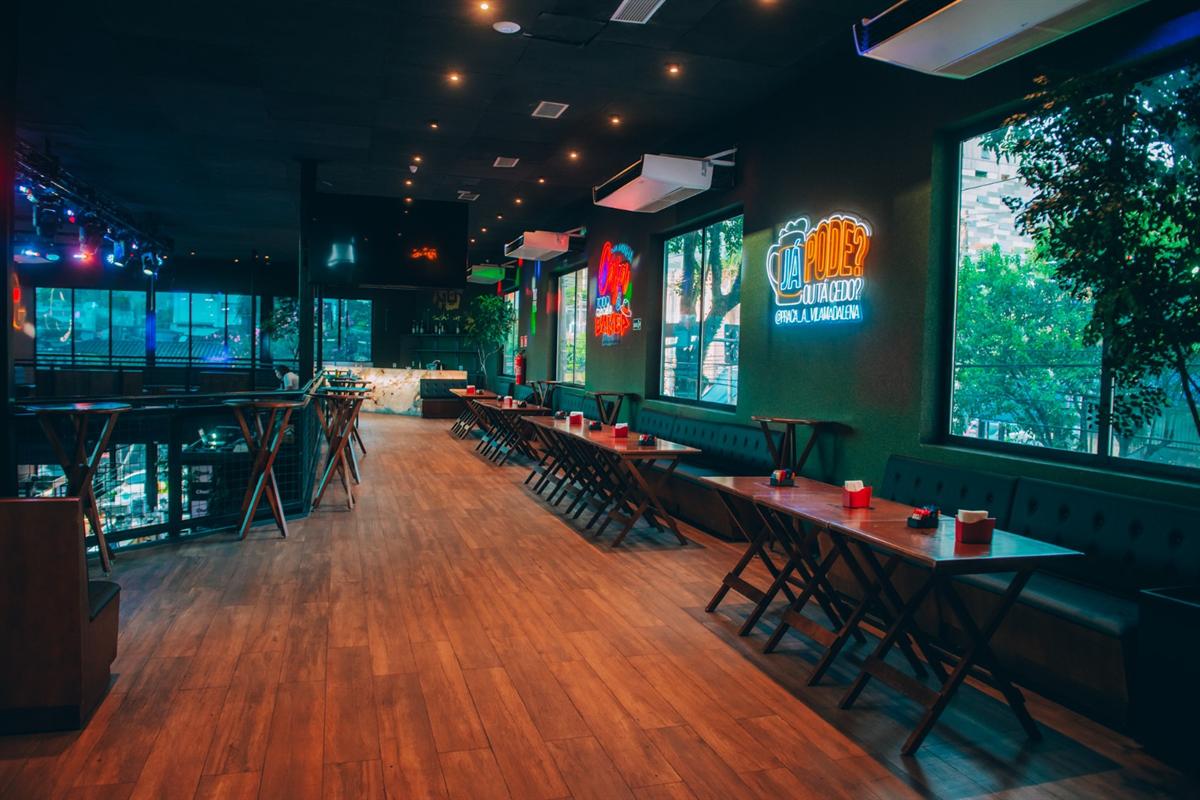 Salão superior com mesas comunitárias e letreiros de neon