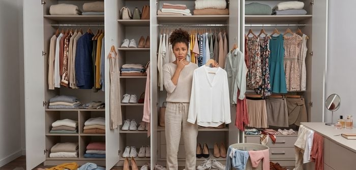 Mulher em frente a um guarda-roupa lotado, sem saber o que vestir