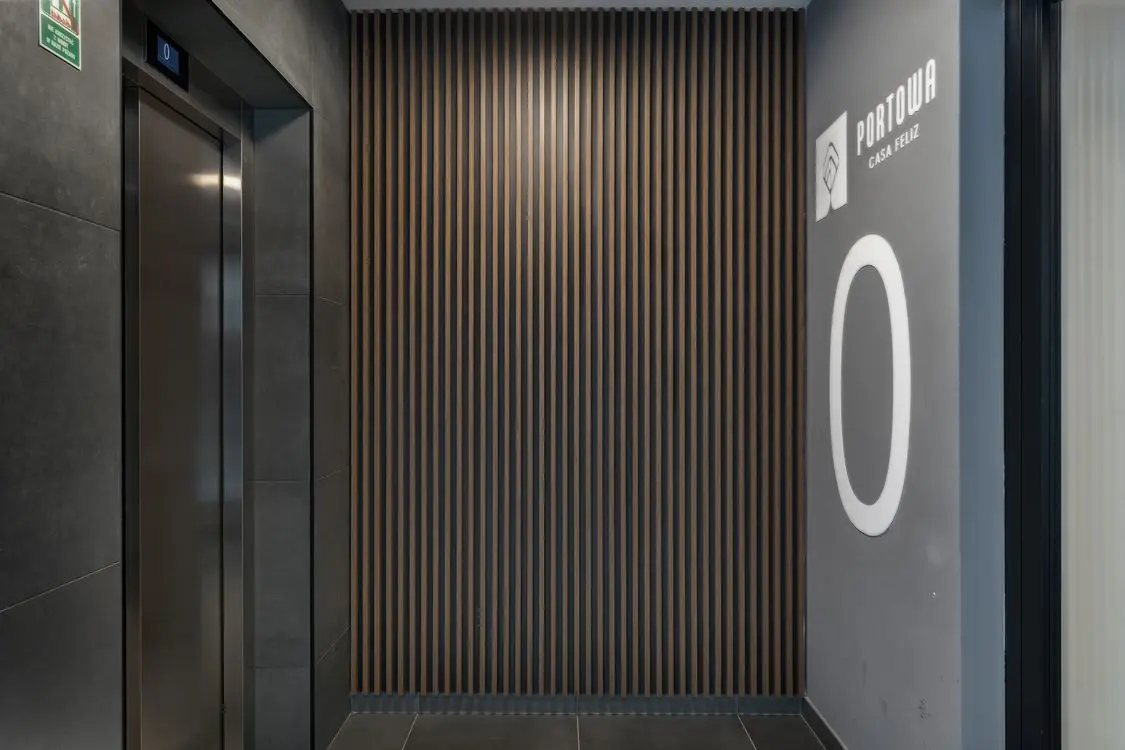 Elevador de aço em hall contemporâneo com paredes cinzas e acabamento em madeira, sem pessoas